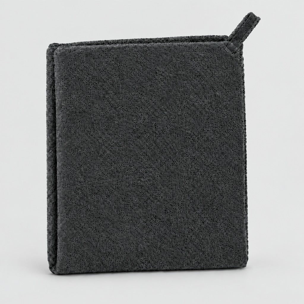 A dark charcoal gray textured cleaning sponge or scrubber with a small loop handle on the top right, shown on a clean light gray background.