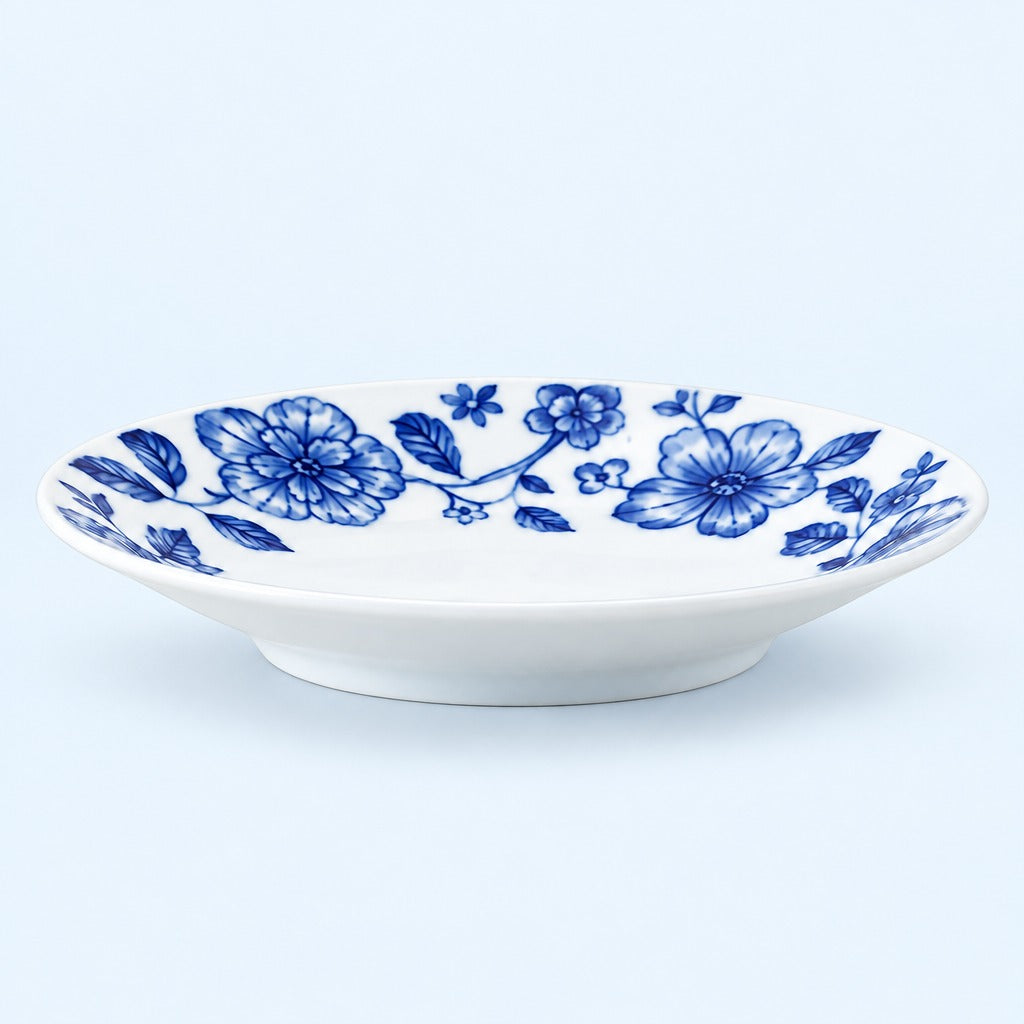 A white ceramic shallow bowl decorated with a blue floral pattern, shown against a light blue background.