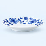 A white ceramic shallow bowl decorated with a blue floral pattern, shown against a light blue background.