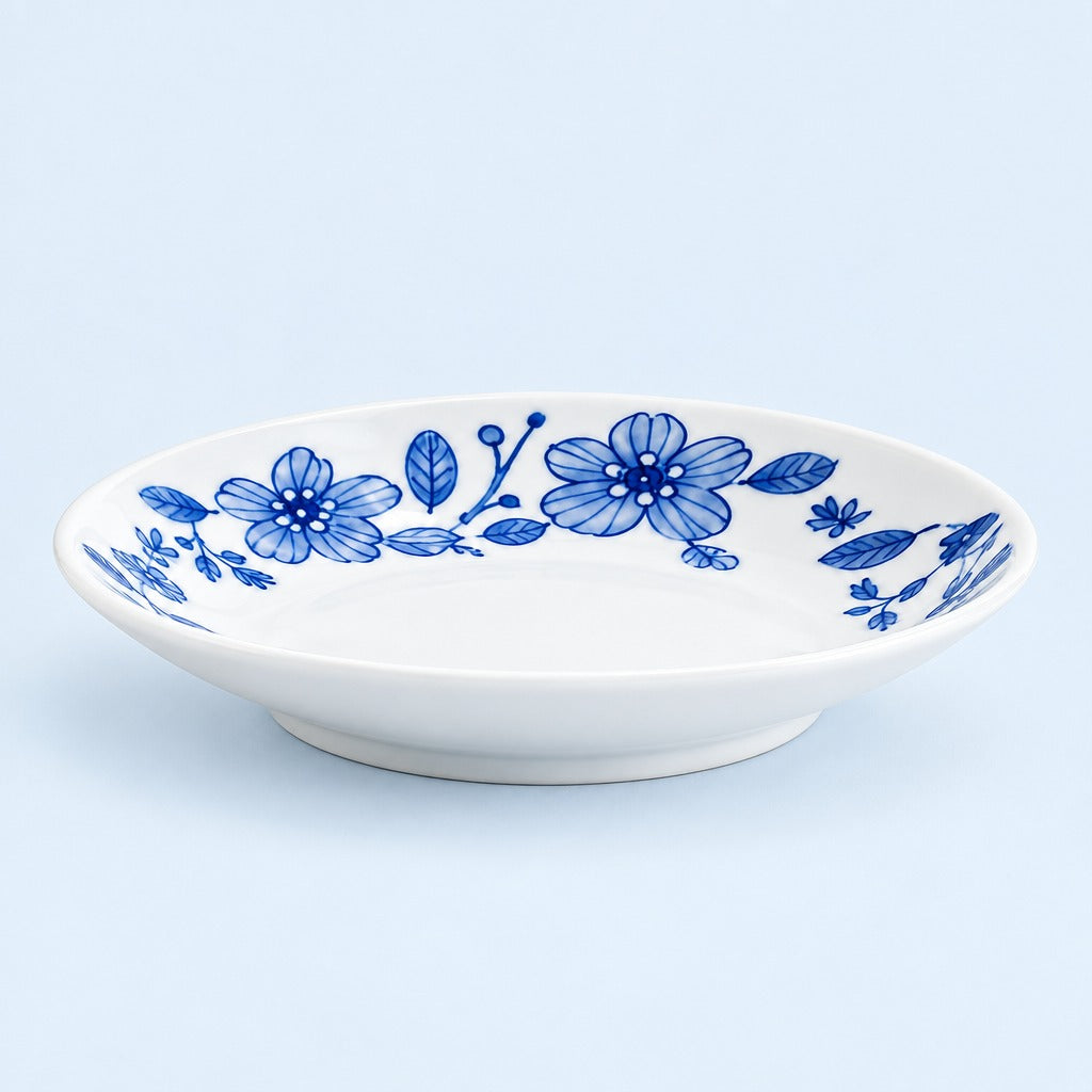 A white ceramic shallow bowl decorated with a blue floral pattern, set against a light blue background.