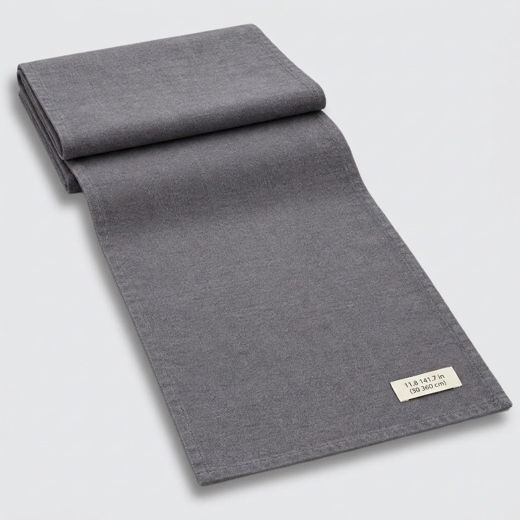 A folded dark gray woven textile, likely a blanket, throw, or scarf, displayed diagonally on a light gray background with a small white fabric label visible in the corner.