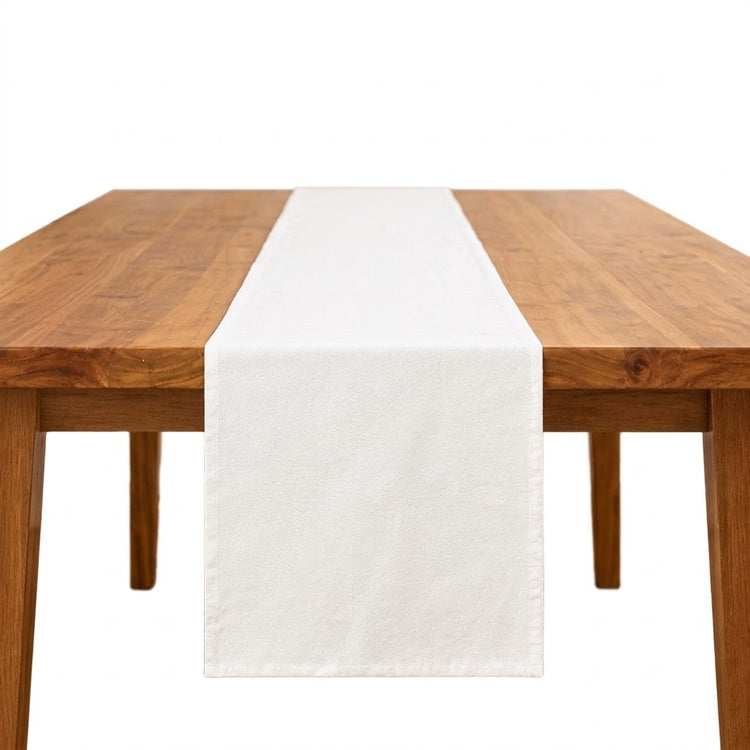 A white fabric table runner centered on a wooden dining table against a plain white background.