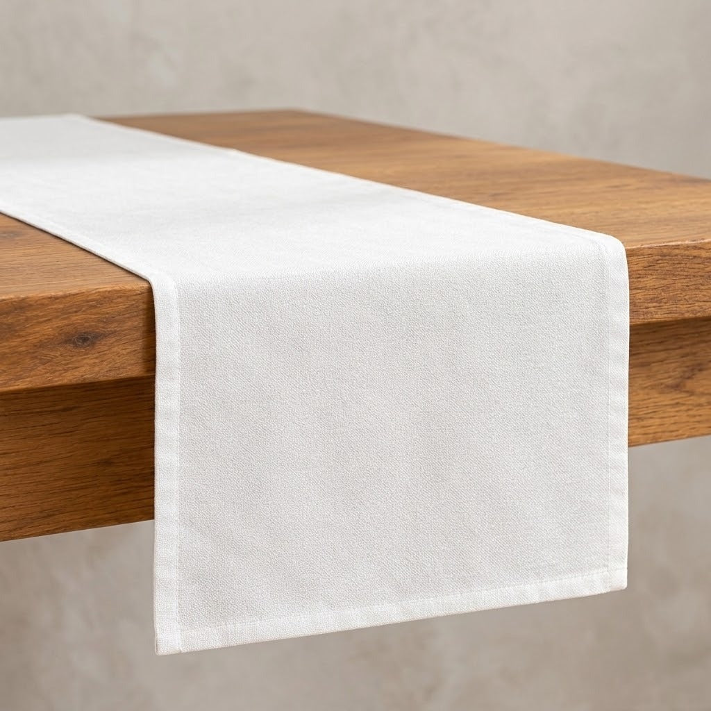A white fabric table runner draped over a wooden table against a neutral textured wall.