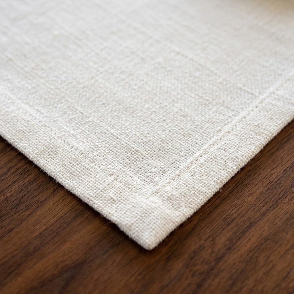 Close-up of a light beige woven textile corner with a stitched border, placed on a dark brown wooden surface.