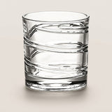 A clear textured glass tumbler with horizontal ridges, photographed on a neutral light beige background.