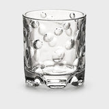 Clear glass tumbler with raised rounded dots and a thick sculpted base stands against a light grey background.