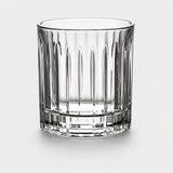 Clear glass tumbler with vertical fluted grooves and a thick round base stands against a light grey background.