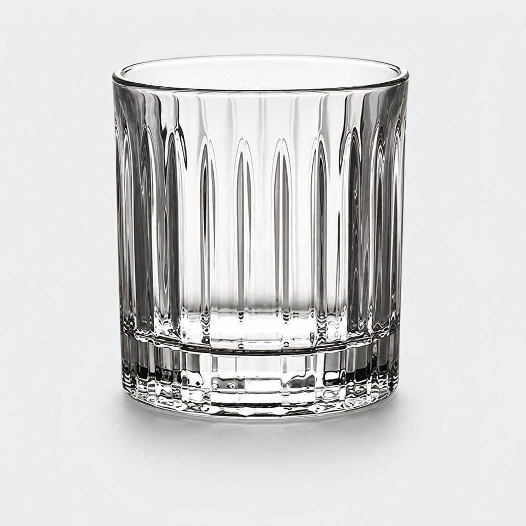 Clear glass tumbler with vertical fluted grooves and a thick round base stands against a light grey background.