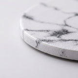A close-up of a round white coaster with a black marble pattern, showing its textured surface and curved edge on a light gray background.