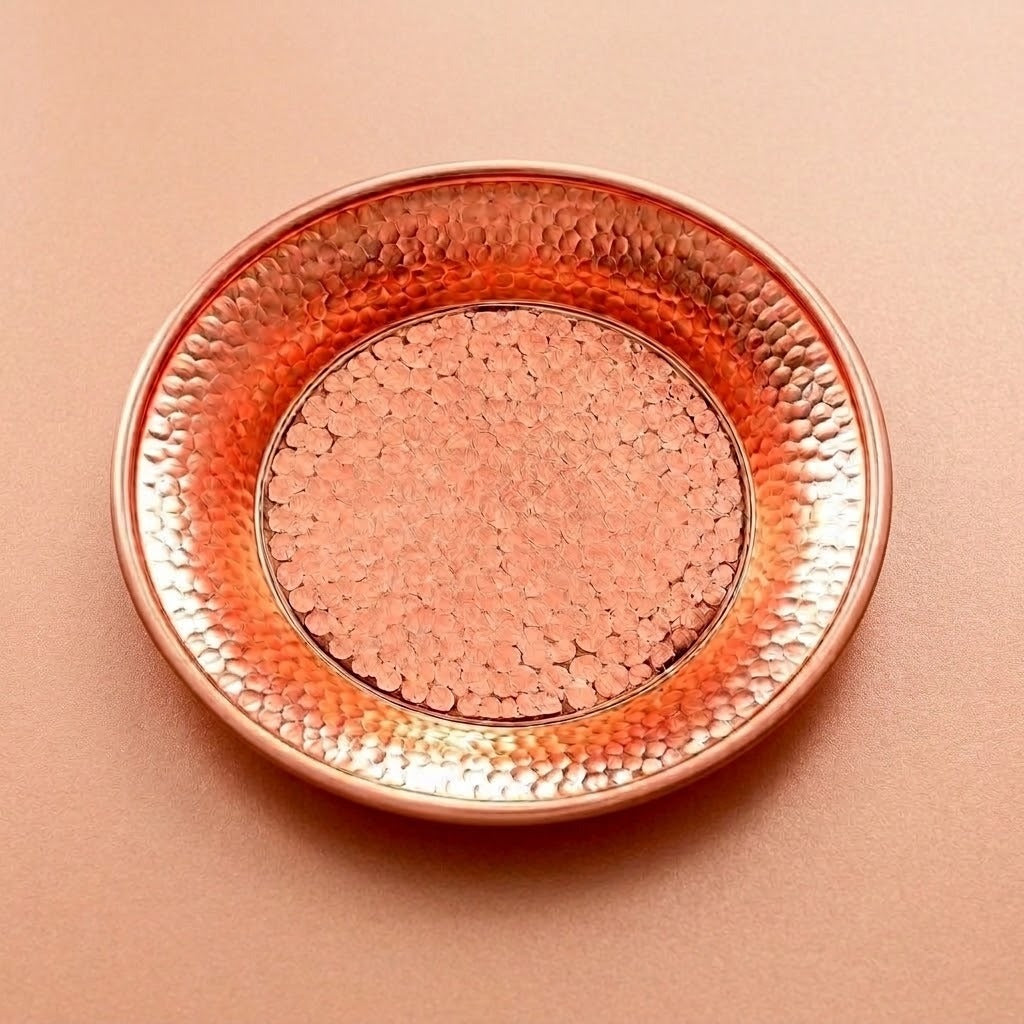 A round hammered metal tray in a warm copper or rose-gold tone, photographed from above on a matching solid background.