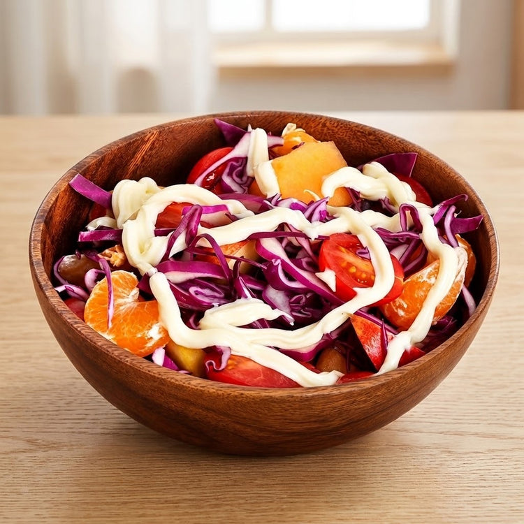 A wooden bowl filled with a colorful salad, including shredded purple cabbage, tomatoes, orange citrus pieces, and a white dressing drizzle, set on a light wood table.