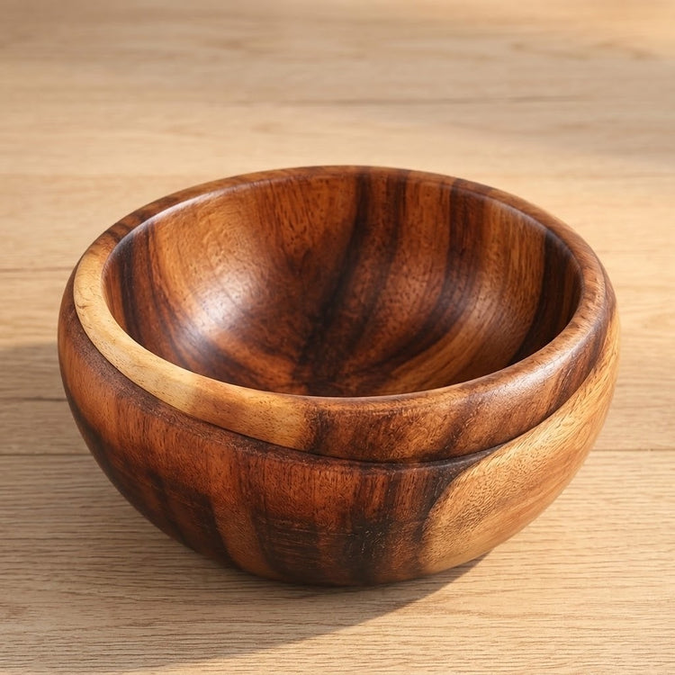 A round wooden bowl with a rich dark brown and warm honey wood grain pattern, resting on a light wood tabletop.