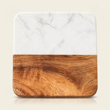 A square serving board or tray with rounded corners, featuring a white marble top half and a warm brown wood grain bottom half, shown on a light beige background.
