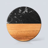 A round split-design coastertop or trivet made of black marble on the top half and natural wood on the bottom half, shown on a light gray background.