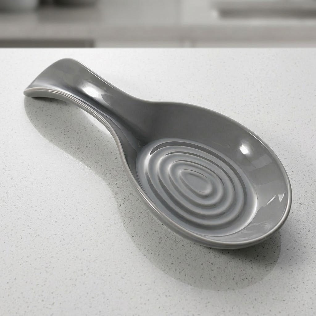 A gray ceramic spoon rest with a ribbed spiral pattern inside the bowl and a curved handle, resting on a light speckled countertop.