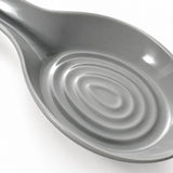 A close-up of a glossy gray ceramic spoon rest with concentric circular ridges inside the bowl, shown on a white background.