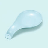 A light blue ceramic spoon rest with a hanging hole, photographed on a matching pale blue background.