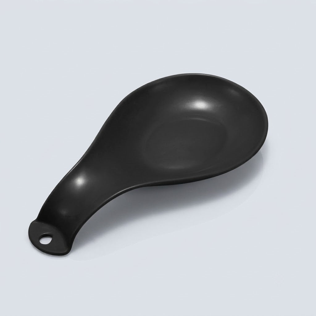 A matte black silicone or rubber spoon rest with a hanging hole at the handle, shown on a light gray background.