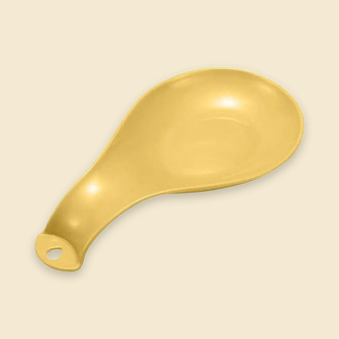 A single gold-colored ceramic spoon rest with a small hanging hole at the handle, shown on a solid light cream background.