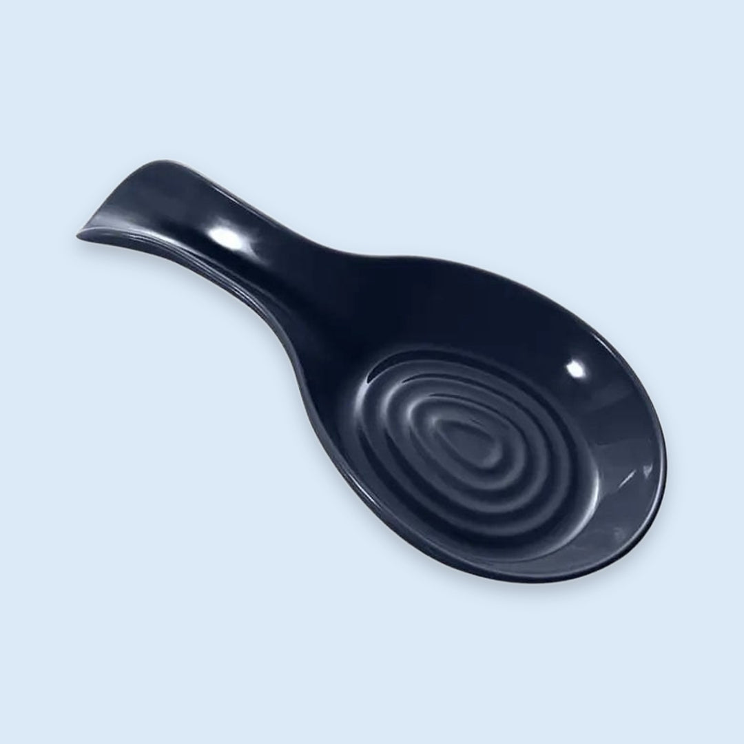 A glossy black ceramic soup spoon rest with a concentric ripple design inside the bowl, shown on a light blue background.