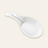 A white ceramic spoon rest with a spiral pattern in the center and a handle on the left, shown on a solid light beige background.