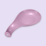A single pink plastic spoon or scoop with a hanging hole at the handle, shown on a plain light lavender background.