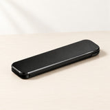 A sleek black rectangular electronic device, possibly a power bank or portable charger, resting diagonally on a light beige wooden surface against a white background.