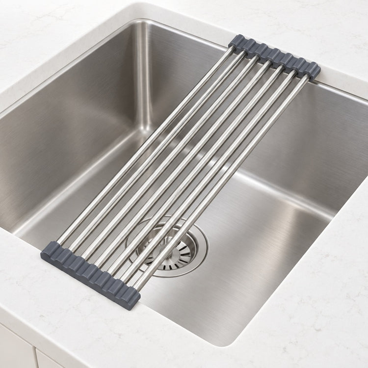 A stainless steel sink drain guard with dark gray rubber end caps, shown resting across a stainless steel kitchen sink.