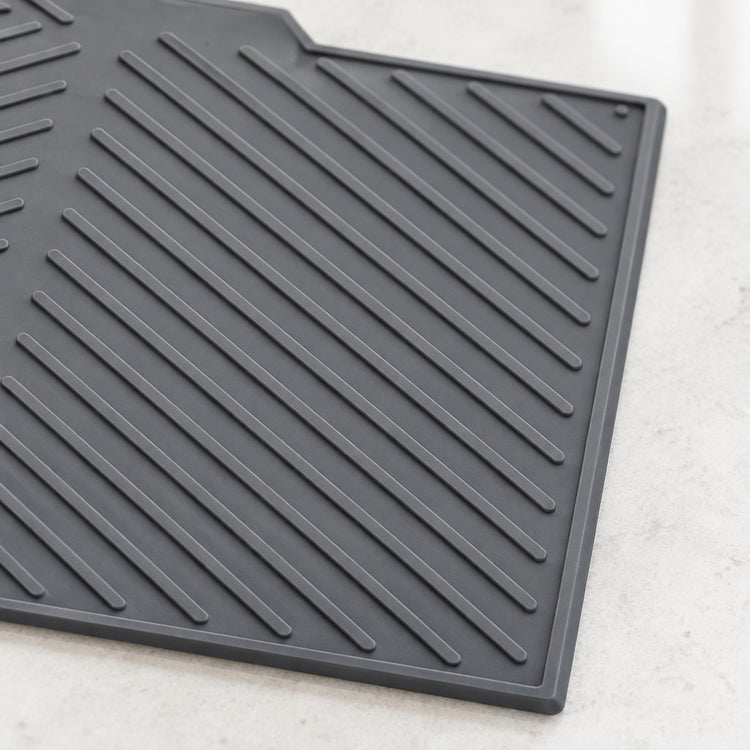 A dark gray rubber kitchen mat with diagonal ridges, shown on a light marble countertop.