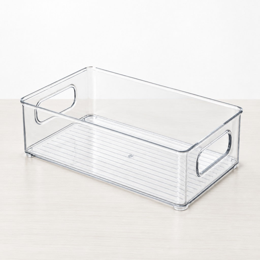 A clear plastic storage bin with integrated side handles and a slotted bottom tray, shown on a light wood surface against a white background.