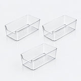 Three clear rectangular storage bins with lowered front openings and dotted bases arranged separately on a white background.