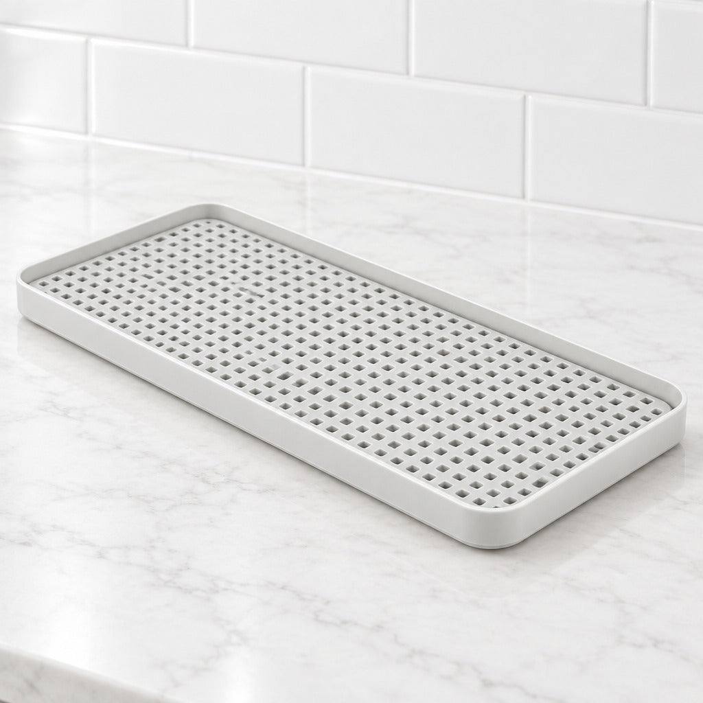 A rectangular white silicone kitchen draining tray with a raised rim and a grid of small drainage holes, shown on a white marble countertop with a white subway tile backsplash.