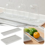 White rectangular kitchen drying rack with a perforated grid surface, shown holding clear drinking glasses and also pictured with vegetables in a kitchen setting. Two additional rack pieces are shown separately on the left, and an inset shows the rack in use on a countertop.
