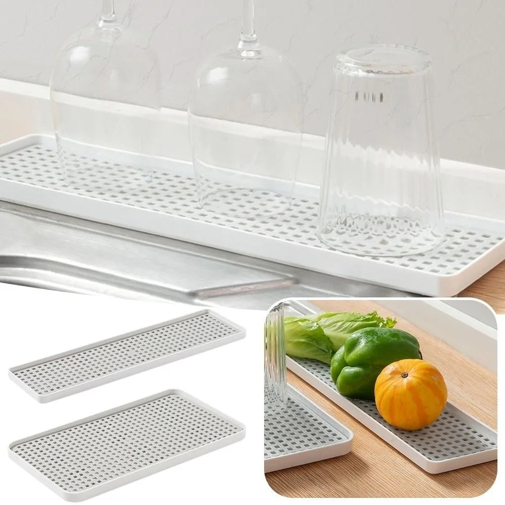 White rectangular kitchen drying rack with a perforated grid surface, shown holding clear drinking glasses and also pictured with vegetables in a kitchen setting. Two additional rack pieces are shown separately on the left, and an inset shows the rack in use on a countertop.