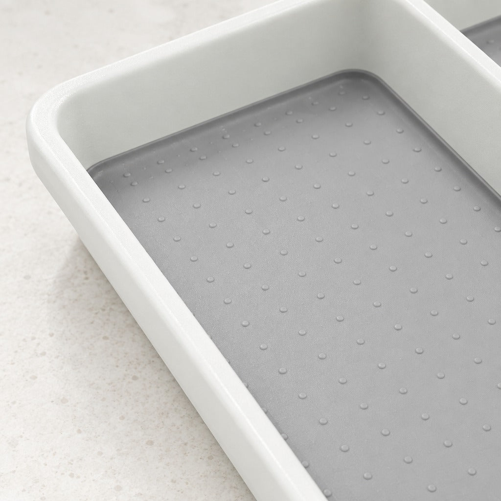 A close-up of a white rectangular tray or container with a gray textured non-slip or anti-static inner liner featuring a grid of small raised dots, set on a light beige speckled countertop.