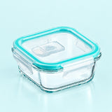 A square clear glass food storage container with a transparent lid and a bright aqua silicone seal, shown on a pale blue background.