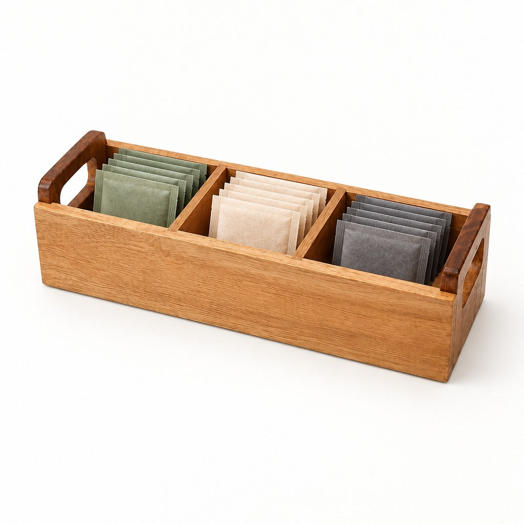 A rectangular wooden tea bag organizer with three compartments holding green, beige, and gray tea bags, shown on a clean white background.