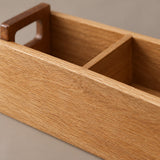 Close-up of a wooden organizer tray with a warm honey oak finish, featuring a rectangular handle cutout on one end and a two-compartment divider.