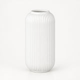 A white ceramic vase with a ribbed, vertically fluted texture, standing on a clean white background.