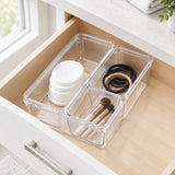 Clear plastic drawer organizer bins arranged inside an open wooden drawer, holding cotton pads, makeup brushes, and hair ties.