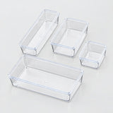 Four clear plastic rectangular storage bins in different sizes arranged on a light gray reflective surface.