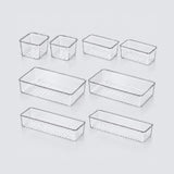Set of eight clear plastic organizer bins in various rectangular sizes with perforated bottoms, arranged on a light gray background.