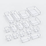 A set of clear plastic rectangular organizer bins in multiple sizes, arranged on a light gray reflective surface.