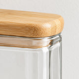 Close-up of a clear glass storage jar with a rounded natural bamboo lid, showing the glass rim and wood grain texture against a light neutral background.