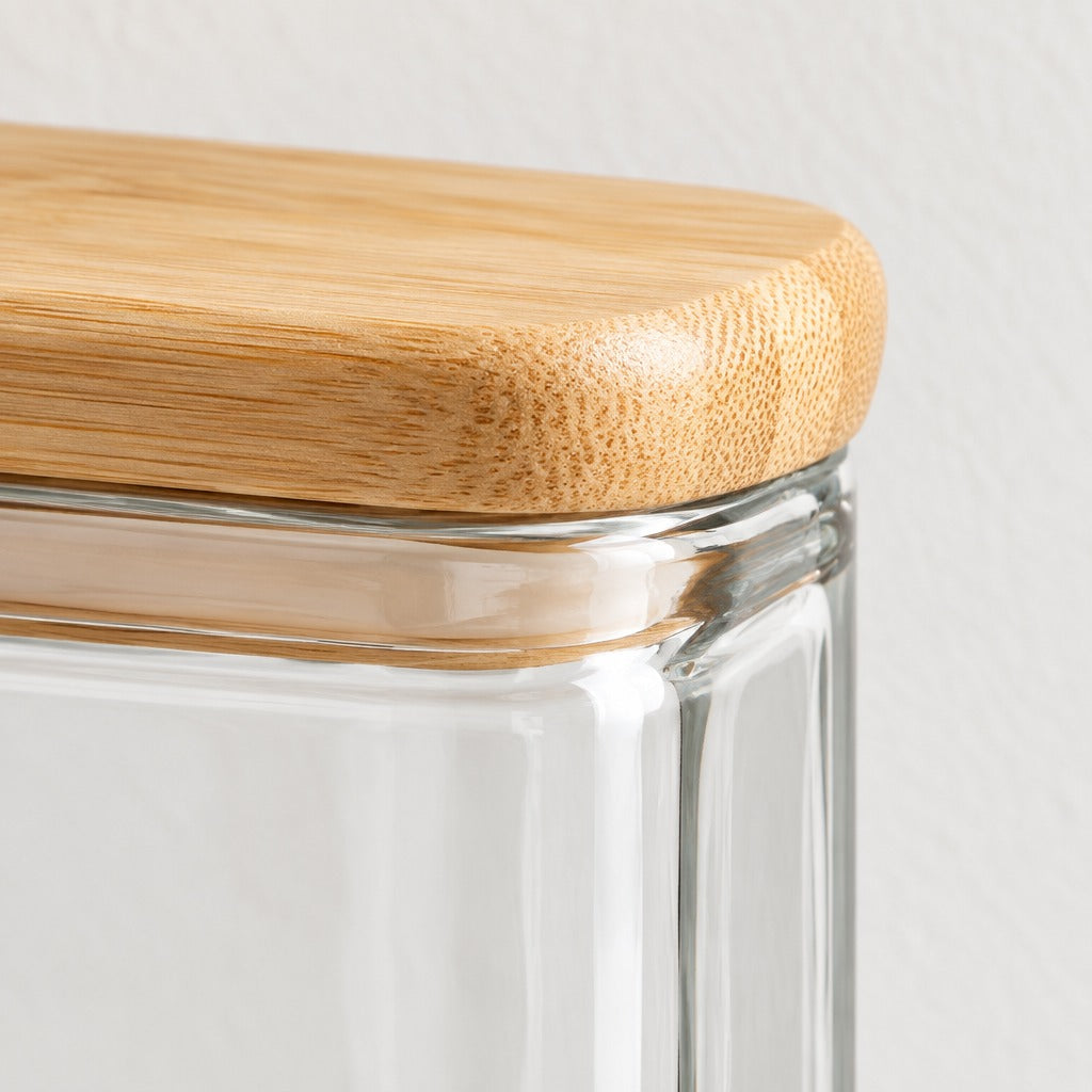 Close-up of a clear glass storage jar with a rounded natural bamboo lid, showing the glass rim and wood grain texture against a light neutral background.