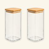Two clear glass canisters with square wooden lids, shown side by side on a light cream background.