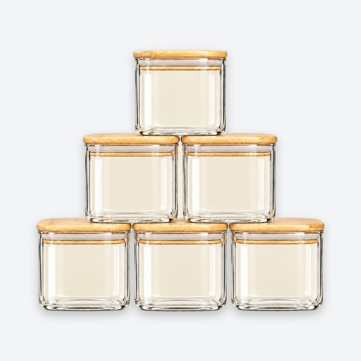 Six clear glass jars with square bases and light natural wood lids, arranged in a pyramid stack on a light gray background.