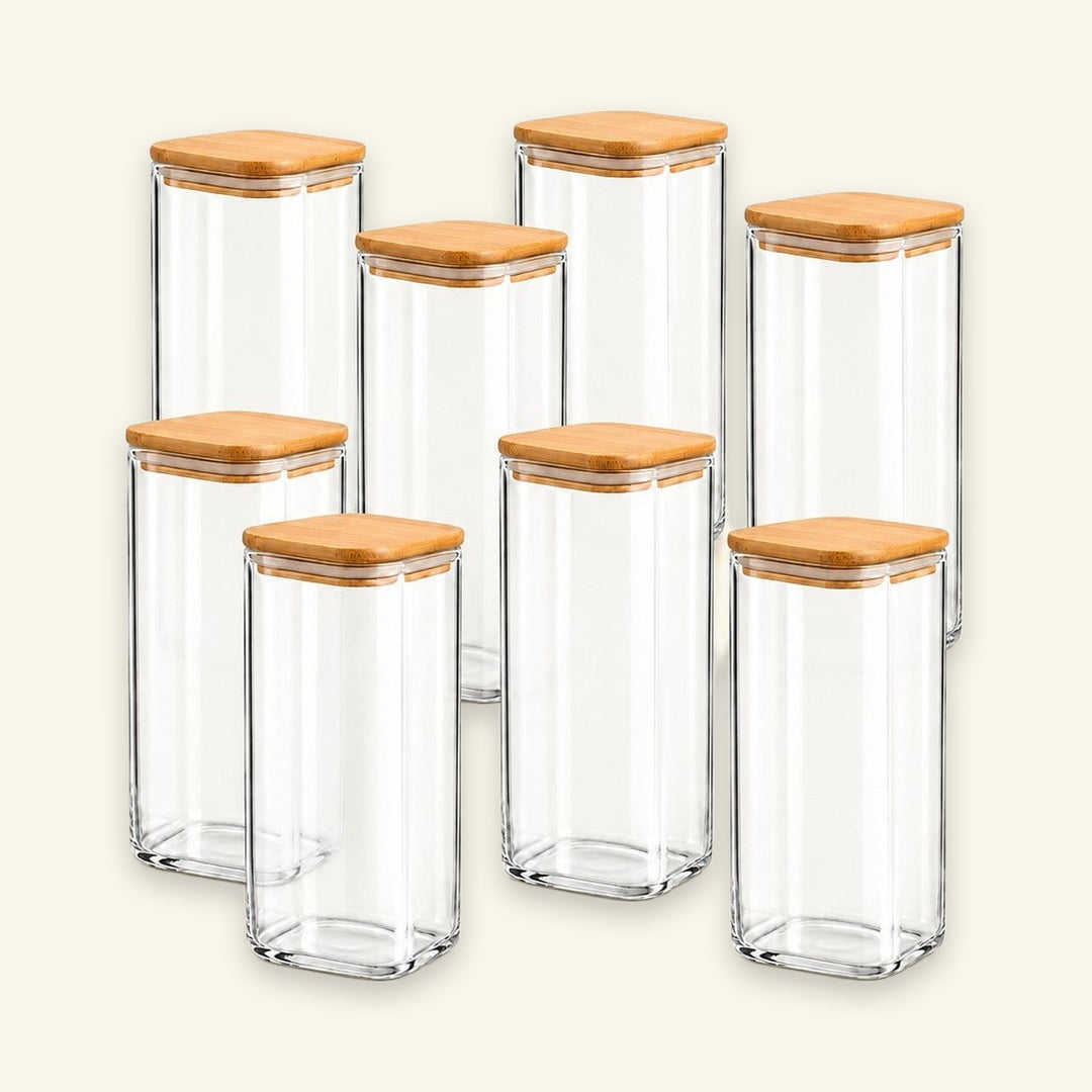 Six clear glass canisters with square bases and light natural wood lids, arranged together on a plain light beige background.