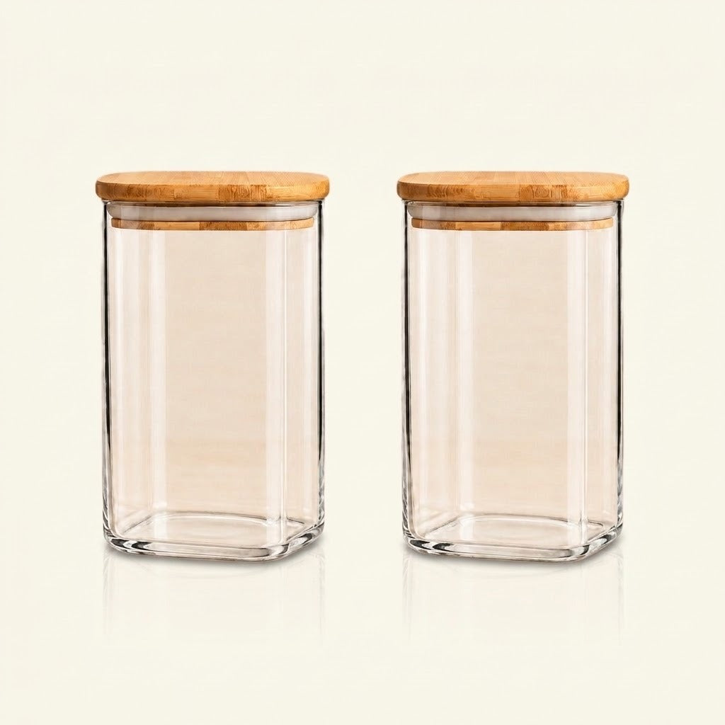 Two clear glass canisters with square bases and light natural wood lids, shown side by side on a plain off-white background.