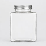 A clear square glass jar with a ribbed silver metal screw-on lid, shown against a plain light gray background.